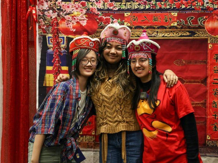 三名学生以红色和金色的中国新年背景摆姿势拍照